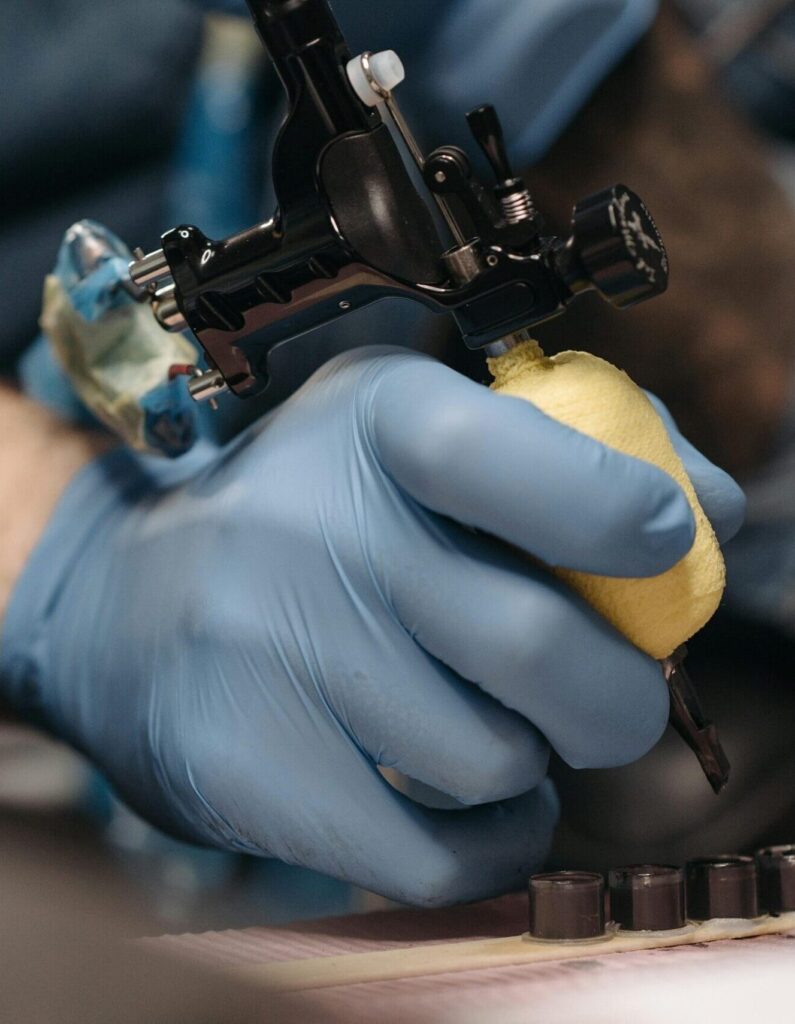 Tattoo artist with gloves operates a tattoo machine in a tattoo parlor setting